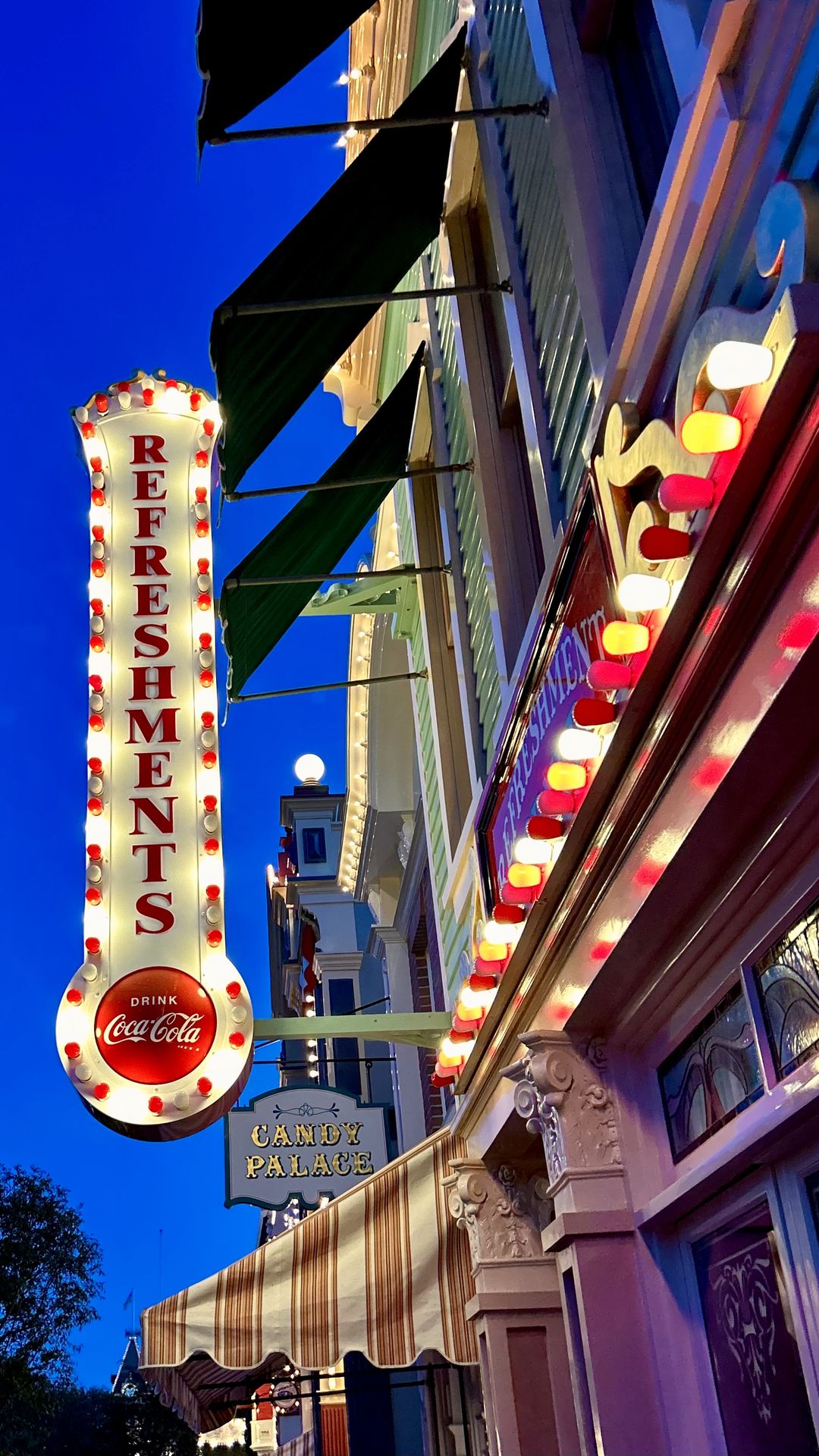 Refreshments and Candy Palace signs glowing against a deep blue sky on Main Street